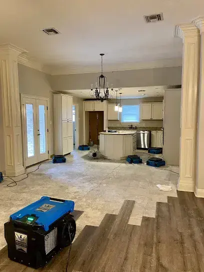 Air movers and a dehumidifier along an open living area with the flooring partly removed