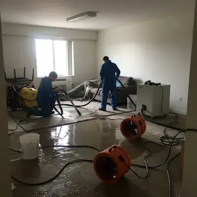 Two technicians extracting water from a wet floor while orange air movers run