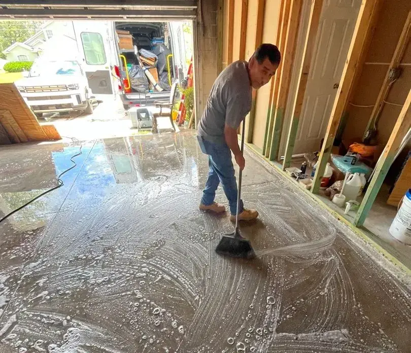 A man sweeping muddy floodwater out of a house toward the open garage door