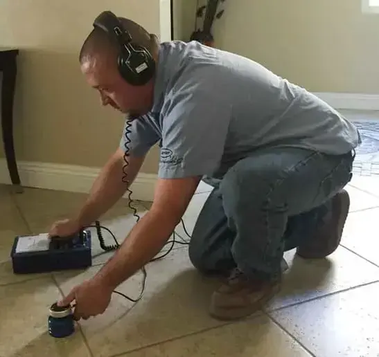 A technician listening with leak detection gear on a tile floor over a slab